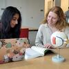 Two students reading from a book with an open laptop on the desk